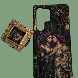 Pu&ograve; includere: Una cover rettangolare per telefono e un supporto quadrato con un'illustrazione scura e ornata di due figure con lunghi capelli fluenti in abiti verdi e dorati. La cover presenta un ritaglio per l'obiettivo della fotocamera.