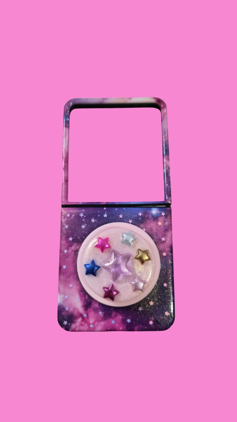 Pu&ograve; includere: Uno specchietto da borsa rettangolare con una stampa galassia blu e viola scuro con piccole stelle bianche. La parte inferiore presenta un inserto circolare in resina trasparente contenente diverse piccole decorazioni a forma di stella.