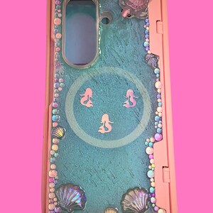 Pu&ograve; includere: Una cover per telefono rosa con un pannello centrale testurizzato color verde acqua e tre piccole sagome di sirene rosa. Il bordo &egrave; decorato con strass iridescenti, vari ciondoli a forma di conchiglia e una piccola tartaruga.