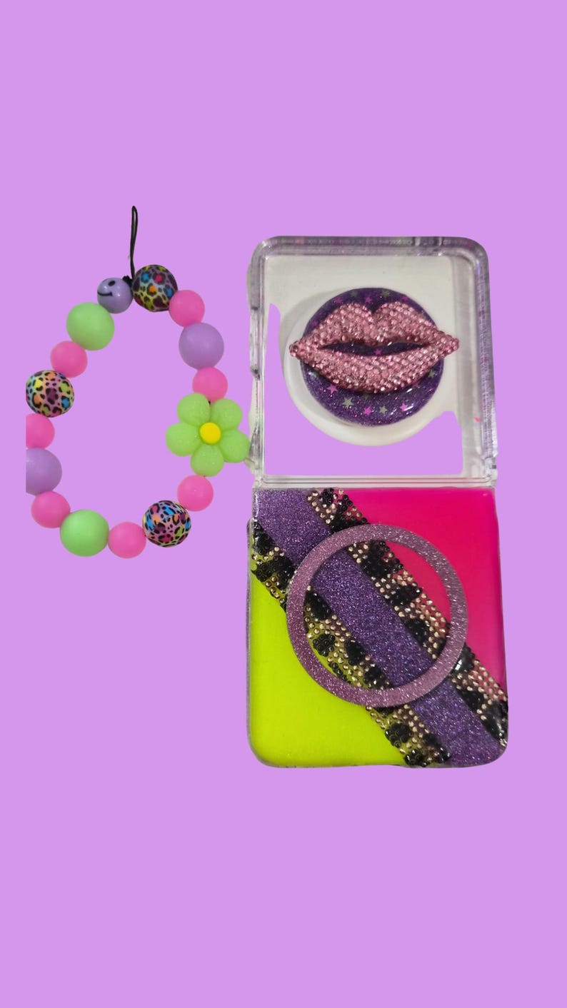 Pu&ograve; includere: Una cover quadrata per telefono con base rosa acceso e giallo neon, caratterizzata da una striscia diagonale glitterata viola, una fascia con stampa leopardata nera e oro e un anello. Un decoro a labbra in strass rosa 3D e un cinturino di perline.