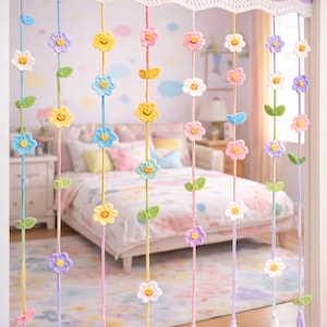 Puede incluir: Cortina de flores de ganchillo con flores sonrientes de colores, hojas verdes y cuerdas de colores pastel. La cortina cuelga frente a una cama, creando un acento de habitación caprichoso y decorativo. Las flores son en tonos de amarillo, azul, rosa y morado.