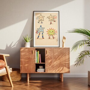 May include: A framed art print featuring four cartoon stars with smiling faces and limbs. The stars are in various poses, with one on roller skates and another with colorful streamers. The artwork is displayed on a wooden cabinet with books and a plant.