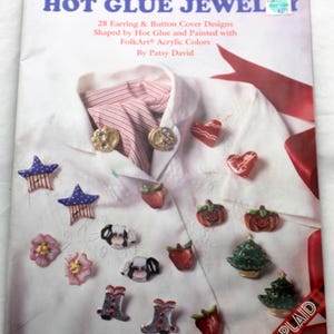 May include: A book titled "Hot Glue Jewelry" featuring a red and white striped scarf and a white shirt with various hot glue jewellery designs. The designs include stars, hearts, pumpkins, apples, boots, and a Christmas tree.