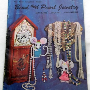 Puede incluir: Un libro de manualidades vintage titulado Bead and Pearl Jewelry con técnicas de macramé, ganchillo y dos agujas. La portada muestra un reloj de pie, dos figuras de ratón y varios collares de cuentas sobre un fondo azul.