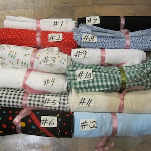 May include: Twelve fabric swatches rolled up and tied with pink ribbon. Each swatch is labeled with a number from 1 to 12. The swatches feature various patterns, including polka dots, gingham, and floral prints.