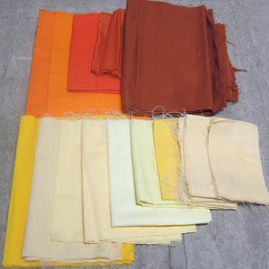 Peut inclure: Une collection de coupons de tissu rectangulaires disposés sur deux rangées. La rangée supérieure présente des nuances d'orange, de rouille et de rouge profond. La rangée inférieure affiche un dégradé de jaune, crème et blanc cassé.