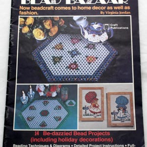 May include: A craft book titled Bead Bazaar by Virginia Jordan featuring 14 bead projects. The cover displays a hexagonal beaded mat, a teapot, and two framed cross-stitch style bead art pieces showing figures with large hats and mailboxes.