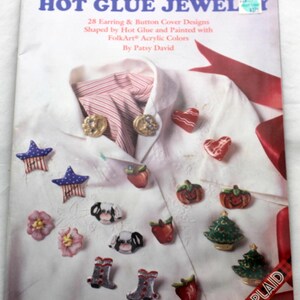 May include: A craft book titled HOT GLUE JEWELRY by Patsy David featuring 28 earring and button cover designs. The cover displays various painted hot glue shapes including stars, hearts, pumpkins, cows, flowers, boots, and trees on a white shirt.