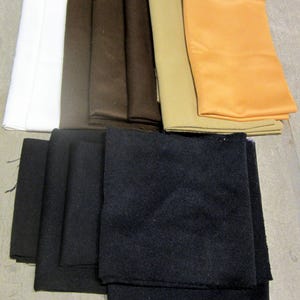 May include: A collection of fabric swatches in various colors, including white, brown, tan, and black. The fabrics appear to be different textures, with some appearing smooth and others more textured. The swatches are neatly stacked, suggesting they are for crafting or design purposes.