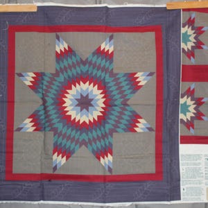 May include: A fabric quilt panel featuring a large central eight-pointed star in shades of teal, red, white, and blue on a gray background. The design includes a red border, a dark blue outer edge with leaf patterns, and additional star motifs.