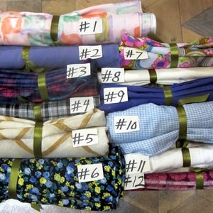 May include: Twelve fabric scraps, each with a different pattern and color, are stacked on top of each other. The scraps are labeled with numbers from 1 to 12. The fabrics include floral prints, plaid, and solid colors.