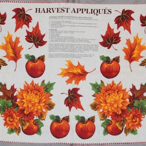 May include: A white fabric panel titled HARVEST APPLIQUÉS featuring printed autumn motifs including orange pumpkins, red apples, green artichokes, and various fall leaves in shades of red, orange, and yellow, with instructional text in the center.