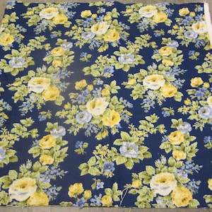 May include: A piece of fabric with a floral pattern. The design features yellow and light blue roses with green leaves on a dark blue background. The fabric has a white edge.