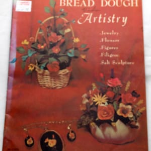 May include: A book titled "Bread Dough Artistry" with a red cover and a picture of a flower arrangement in a basket. The book cover also lists the types of crafts that can be made with bread dough, including jewelry, flowers, figures, filigree, and salt sculpture.