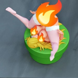 Könnte beinhalten: Eine Sammlerfigur mit einer blonden Figur mit langem Haar, die auf einem runden grünen Sockel steht. Die Figur trägt weiße, gerüschte Beinwärmer und ist in einer liegenden Pose mit nach oben gestreckten Beinen dargestellt.