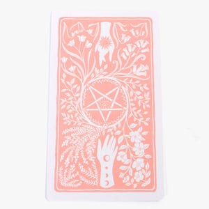 May include: A tarot card with a peach background and white illustrations. The design features a central pentagram, hands, flowers, and celestial symbols. The card has a white border.