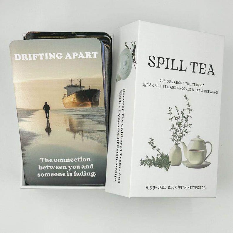 May include: A deck of cards titled "DRIFTING APART" with an image of a person on a beach and a ship. The box reads "SPILL TEA" and "Uncover The Unfiltered Truths And Hidden Dynamics Of Relationships". The deck is an 80-card deck with keywords.