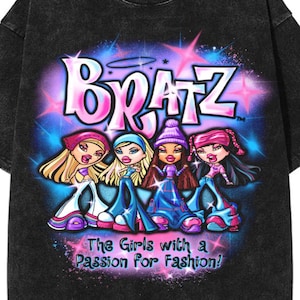May include: Black washed color t-shirt featuring a graphic of four Bratz dolls with the word "Bratz" in pink and blue. The text "The Girls with a Passion For Fashion!" is below the dolls. The shirt has short sleeves and a crew neck.