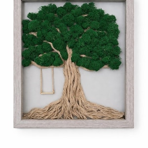 May include: A framed artwork featuring a tree design. The tree's foliage is made of green moss, with a trunk and roots crafted from natural twine. A small swing hangs from a branch. The frame is a light gray color.