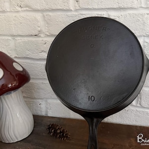 May include: A black cast iron skillet with the text "WAGNER" and "SIDNEY O." stamped on the bottom. The number "10." is also visible. Decorative mushroom figurines are in the background.
