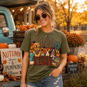 Puede incluir: Una camiseta verde oliva con un estampado gráfico con el texto Vet Tech. El diseño incluye un golden retriever, un gato, un conejo y un bulldog francés rodeados de calabazas, girasoles, un estetoscopio y una pila de libros.