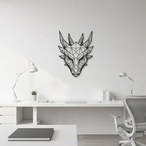 Puede incluir: Una obra de arte mural con forma de cabeza de dragón geométrica negra. La cabeza del dragón está hecha de líneas interconectadas, creando un diseño poligonal. La obra está montada en una pared blanca, encima de un escritorio blanco.