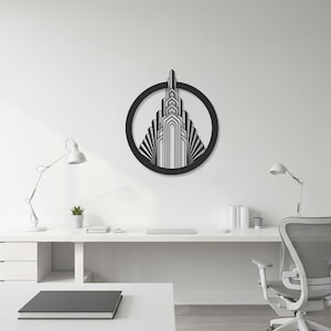 May include: Black metal wall art depicting an Art Deco skyscraper within a circular frame. The artwork is mounted on a white wall above a white desk, creating a modern office aesthetic. The design includes geometric patterns and vertical lines.