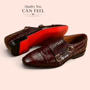 Pode incluir: Um par de sapatos de fivela dupla em castanho escuro com textura de crocodilo, fivelas douradas e solas vermelho-brilhante. O texto "Quality You CAN FEEL" e "KINGSMANHIDE" com um ícone de coroa é visível acima do calçado.