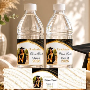 Könnte beinhalten: Zwei transparente Wasserflaschen mit weißen Verschlüssen. Jede Flasche hat ein Etikett mit einem Foto einer Absolventin in Robe und Hut, dem Text "Graduate Olivia Smith Class of 2026" und goldenen und schwarzen Akzenten. Thema: Abschlussfeier.