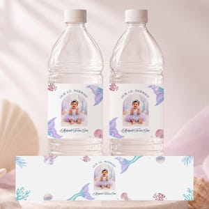 May include: Two clear plastic water bottles and a flat label featuring a photo of a baby in a tutu, surrounded by watercolour illustrations of mermaid tails, coral, and seashells. The text reads Our Lil Mermaid and Aaliyah Turns One.