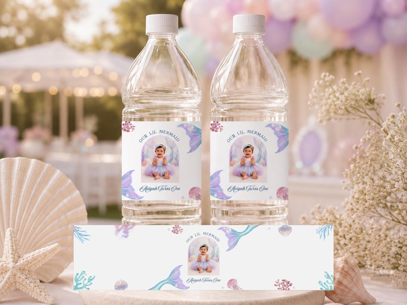 May include: Two clear plastic water bottles with custom labels featuring a photo of a child, the text Our Lil Mermaid and Aaliyah Turns One, decorated with watercolour illustrations of mermaid tails, seashells, and coral in shades of purple and blue.