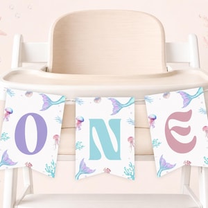 May include: A three-piece decorative banner featuring the word ONE in large, colorful letters. Each white pennant displays a watercolor illustration of a mermaid tail, jellyfish, and coral in shades of purple, blue, and pink on a white background.
