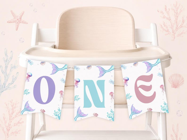 May include: A three-piece decorative banner featuring the word ONE in large, colorful letters. Each white pennant displays a watercolor illustration of a mermaid tail, jellyfish, and coral in shades of purple, blue, and pink on a white background.