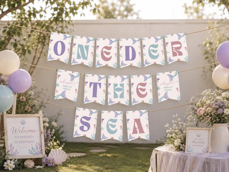 K&ouml;nnte beinhalten: Ein dekoratives Banner-Set bestehend aus einzelnen Wimpeln mit einem Meerjungfrauen- und Meeresmuster. Die Buchstaben bilden den Schriftzug ONEDER THE SEA in Lila, Blau und Pink. Jeder Wimpel hat ein spitzes Ende und h&auml;ngt an einer d&uuml;nnen Schnur.
