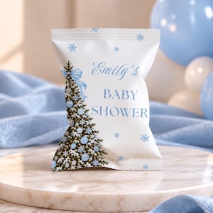 May include: A white snack bag featuring a printed design of a Christmas tree decorated with light blue ornaments and a blue bow. The text reads Emily's BABY SHOWER in blue, surrounded by light blue snowflake illustrations on the bag surface.