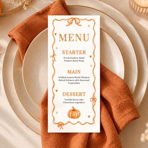 Könnte beinhalten: Eine vertikale rechteckige Menükarte mit einem orangefarbenen Bandrand, die den Text MENU, STARTER, MAIN und DESSERT enthält. Das Menü listet Fresh Garden Salad, Tomato Basil Soup, Grilled Lemon Herb Chicken, Baked Salmon, Vanilla bean cake und Chocolate cupcakes auf.
