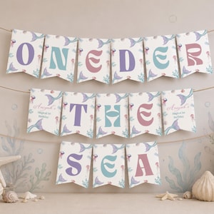 K&ouml;nnte beinhalten: Ein dekoratives Banner mit drei Reihen von Wimpeln, die an einer Schnur h&auml;ngen. Die Wimpel zeigen den Text ONEDER THE SEA in violetten, t&uuml;rkisfarbenen und rosafarbenen Buchstaben, verziert mit Illustrationen von Meerjungfrauenschw&auml;nzen und Quallen.