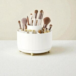 Op de afbeelding: Een witte, geribbelde, roterende make-up organizer met goudkleurige voetjes. De organizer is gevuld met diverse make-up kwasten, lippenstiften en andere beautyproducten. Het heeft meerdere compartimenten.