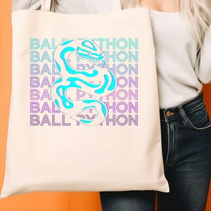 K&ouml;nnte beinhalten: Cremefarbene Tragetasche mit einer t&uuml;rkisfarbenen und wei&szlig;en Schlange. Die Worte "BALL PYTHON" sind vertikal in einem T&uuml;rkis- und Lila-Farbverlauf gestapelt. Ein Reptilien-Themen-Design.
