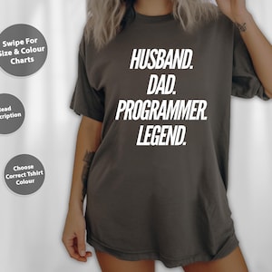 May include: A dark grey t-shirt with the words "HUSBAND. DAD. PROGRAMMER. LEGEND." in white block letters. The shirt has a relaxed fit and short sleeves. The image also includes three grey circular buttons with text.