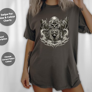 May include: Dark grey t-shirt with a detailed skull graphic wearing goggles and a breathing apparatus. The design is in shades of grey and white, with a tribal-style flame design at the bottom. The shirt also has text on the left side: "Swipe For Size & Colour Charts", "Read Description", and "Choose Correct Tshirt Colour".