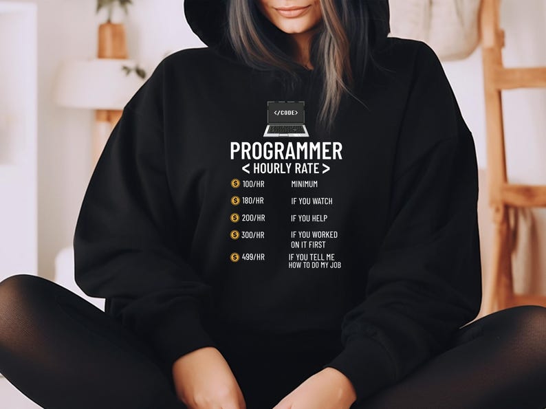 May include: Black hoodie featuring the text "PROGRAMMER < HOURLY RATE >" and a laptop graphic. The text lists hourly rates from &pound;100/HR to &pound;499/HR, with conditions like "IF YOU WATCH" and "IF YOU TELL ME HOW TO DO MY JOB."