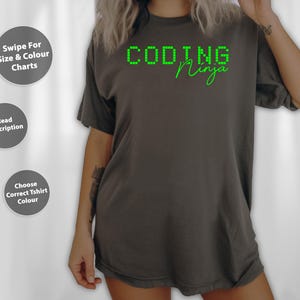 May include: Dark grey t-shirt with the words "CODING Ninja" in green. The word "CODING" is in a pixelated font, and "Ninja" is in a handwritten style. The shirt is a casual style.