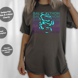 May include: Dark grey t-shirt featuring a turquoise and purple snake graphic and the words "BALL PYTHON". The shirt has a relaxed fit. Additional text on the image includes "Swipe For Size & Colour Charts", "Read Description", and "Choose Correct Tshirt Colour".