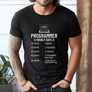 May include: Black t-shirt with the word "PROGRAMMER" and "< HOURLY RATE >" printed in white. The shirt lists hourly rates from &pound;79/HR to &pound;395/HR with corresponding descriptions. A laptop graphic is above the text.
