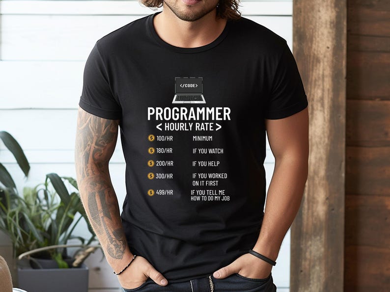 May include: Black t-shirt with the word "PROGRAMMER" and "< HOURLY RATE >" printed in white. The shirt lists hourly rates from &pound;79/HR to &pound;395/HR with corresponding descriptions. A laptop graphic is above the text.
