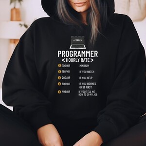 Peut inclure: Sweat &agrave; capuche noir avec l'inscription "PROGRAMMER < HOURLY RATE >" et un graphique d'ordinateur portable. Le texte indique des tarifs horaires de 100&euro;/heure &agrave; 499&euro;/heure avec des conditions. Un design humoristique pour les d&eacute;veloppeurs.