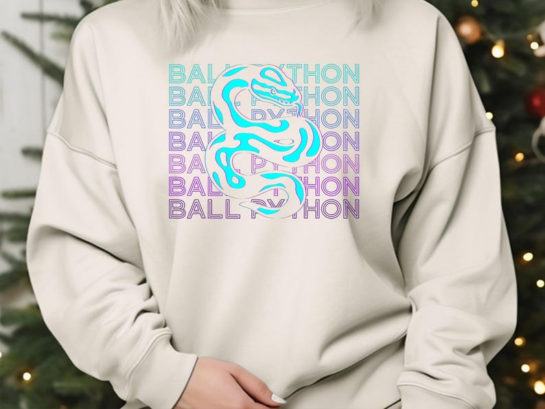 K&ouml;nnte beinhalten: Cremefarbenes Sweatshirt mit einem t&uuml;rkisfarbenen und wei&szlig;en Schlangenmuster und dem Text "BALL PYTHON" in einem sich wiederholenden Muster. Die Schlange ist stilisiert und der Text hat einen blauen und violetten Farbverlauf.