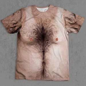 May include: A short-sleeve crew neck t-shirt featuring a realistic, high-resolution photographic print of a human torso with light skin tones and dark, dense chest hair covering the center of the chest and extending toward the shoulders.