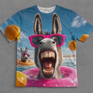 Könnte beinhalten: Ein kurzärmeliges T-Shirt mit einem vollfarbigen Grafikdruck eines Esels mit weit geöffnetem Maul, der eine leuchtend rosa Sonnenbrille trägt. Der Esel schwimmt in einem rosa Schwimmreifen im Meer, umgeben von orangefarbenen Strandbällen.